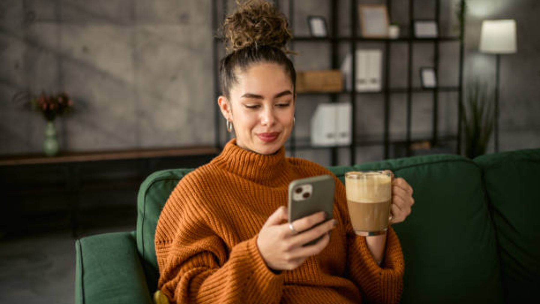 Mujer tomando café en casa y mirando su móvil.