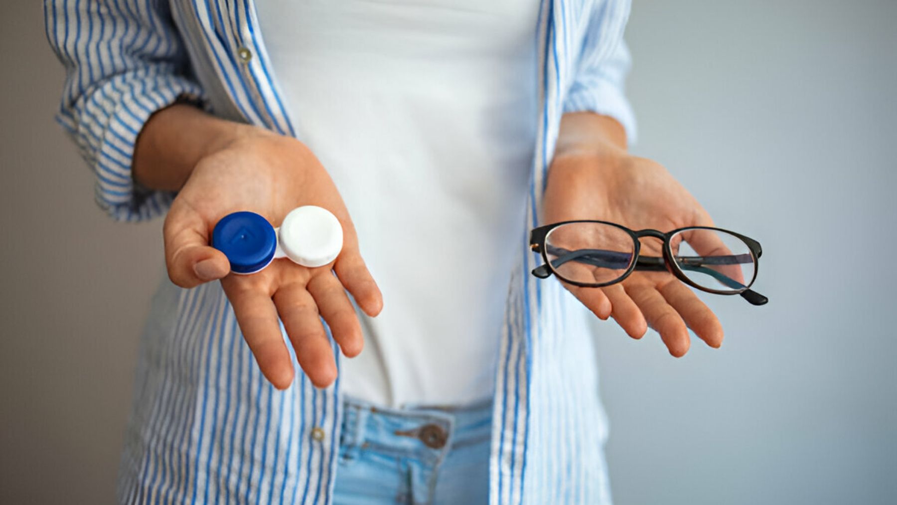 Mujer sostiene lentillas en una mano y gafas en la otra.