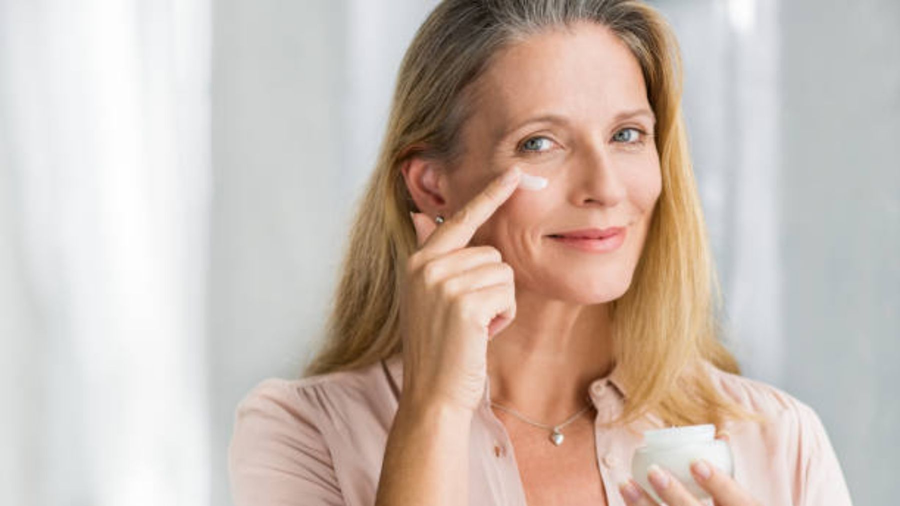 Mujer madura aplicando crema en su rostro.