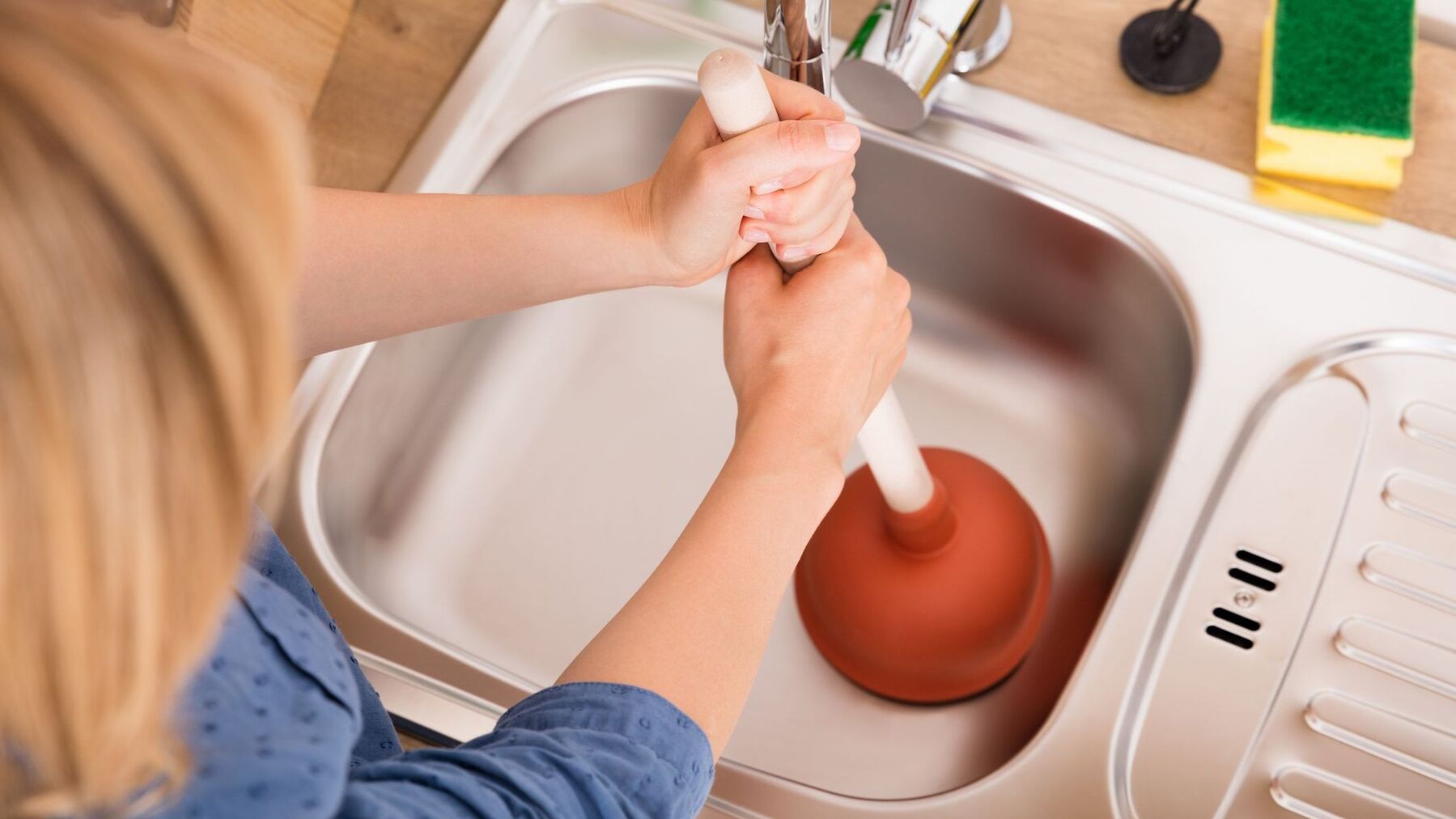 High Angle View Of Woman Using Plunger In Sink