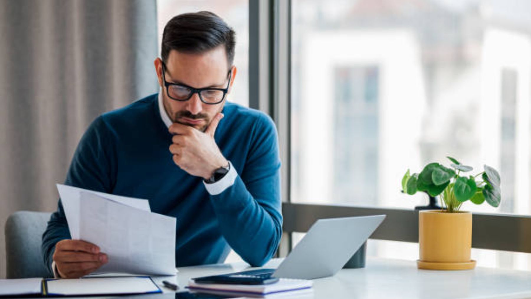 Hombre ejecutivo con su portátil leyendo un documento.