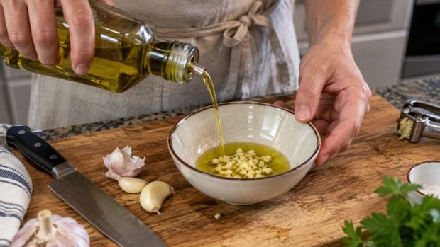 Pelamos y picamos un diente de ajo o dos, dependiendo de cu&aacute;nto nos guste este ingrediente. Lo ponemos en un bol con aceite de oliva.