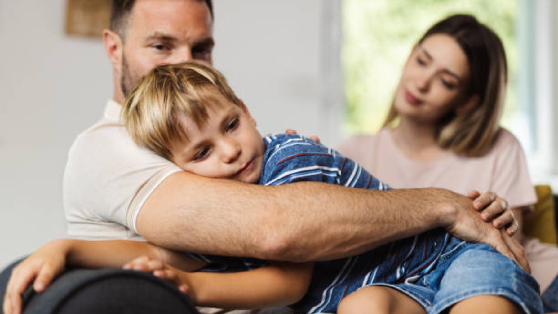 Padre consolando a su hijo con madre de fondo.