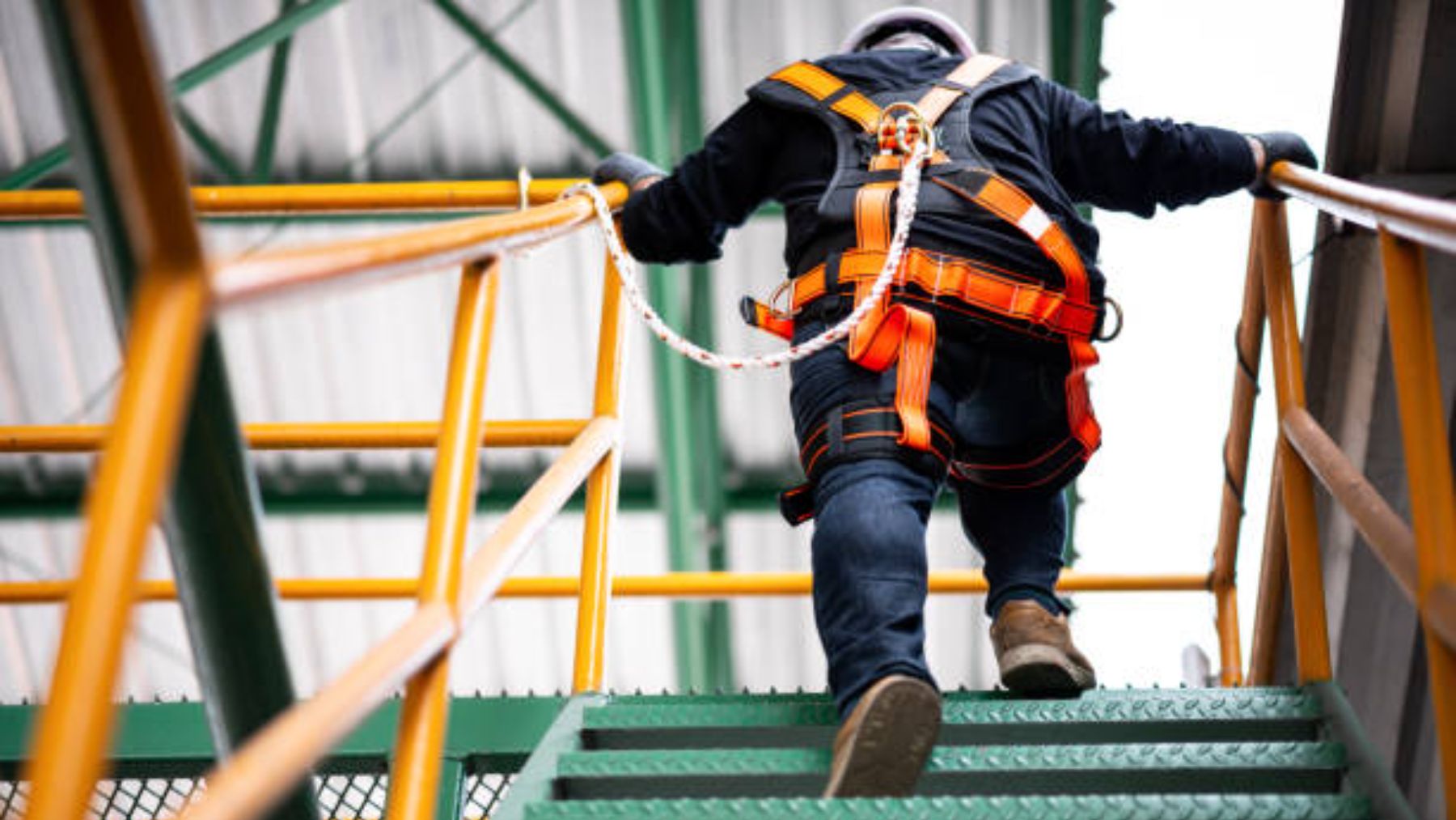 Trabajador sube escalera con arnés.