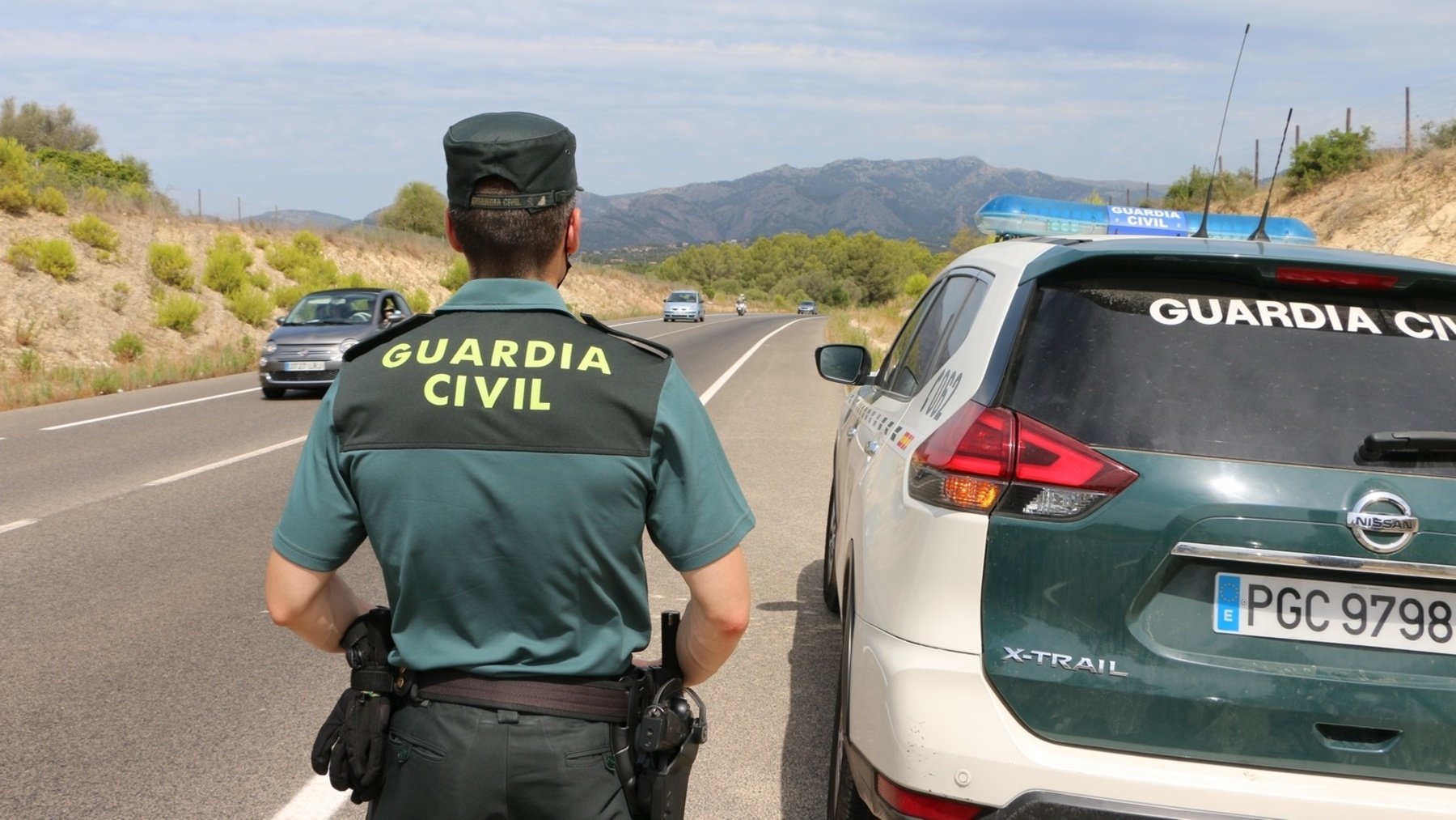 Un agente de la Guardia Civil junto a un vehículo patrulla.