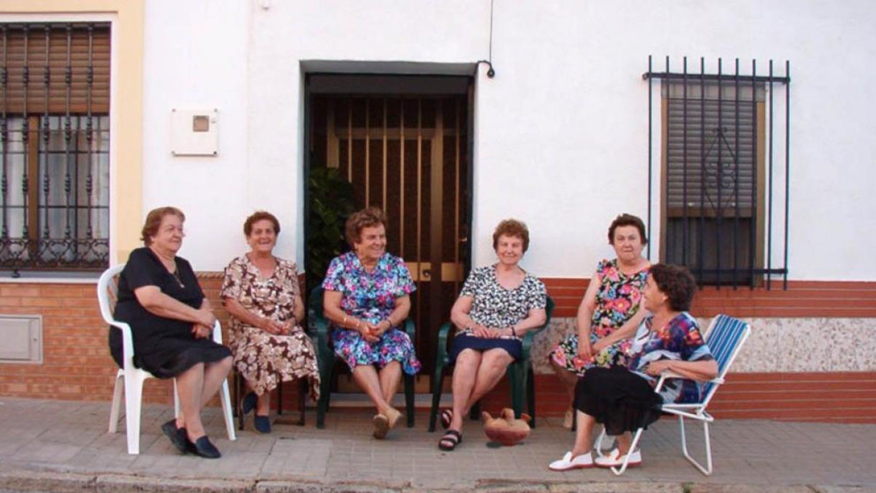 Mujeres en sus sillas frente a sus casas en una foto antigua.