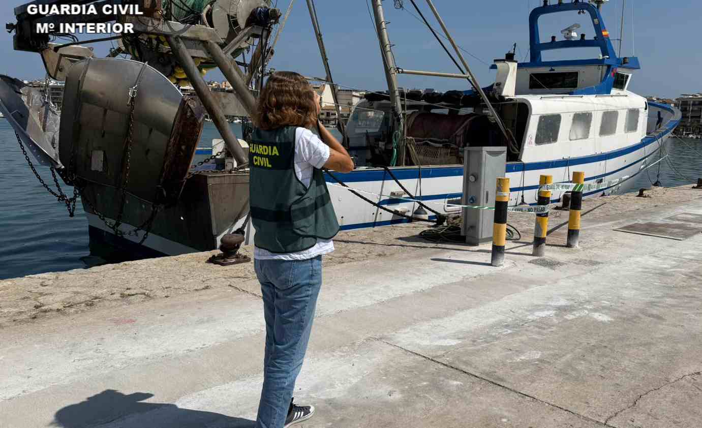 Una agente de la Guardia Civil con el pesquero que sufrió el incendio.