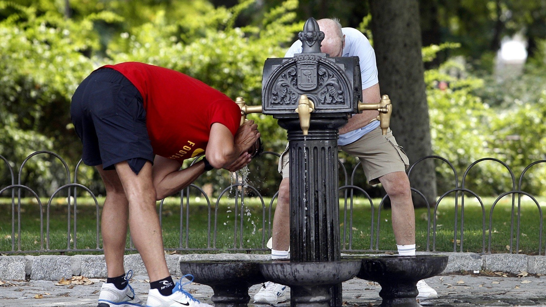 Dos personas se refrescan en una fuente. (EP)