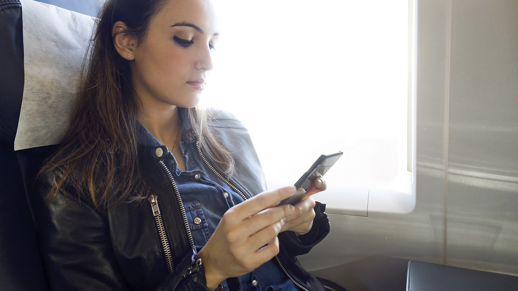 Mujer usando su teléfono en el avión. Foto: Freepik.