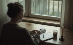 Persona reflexionando con un cuaderno junto a una ventana, simbolizando la duda antes de plantearse un amarre de amor.