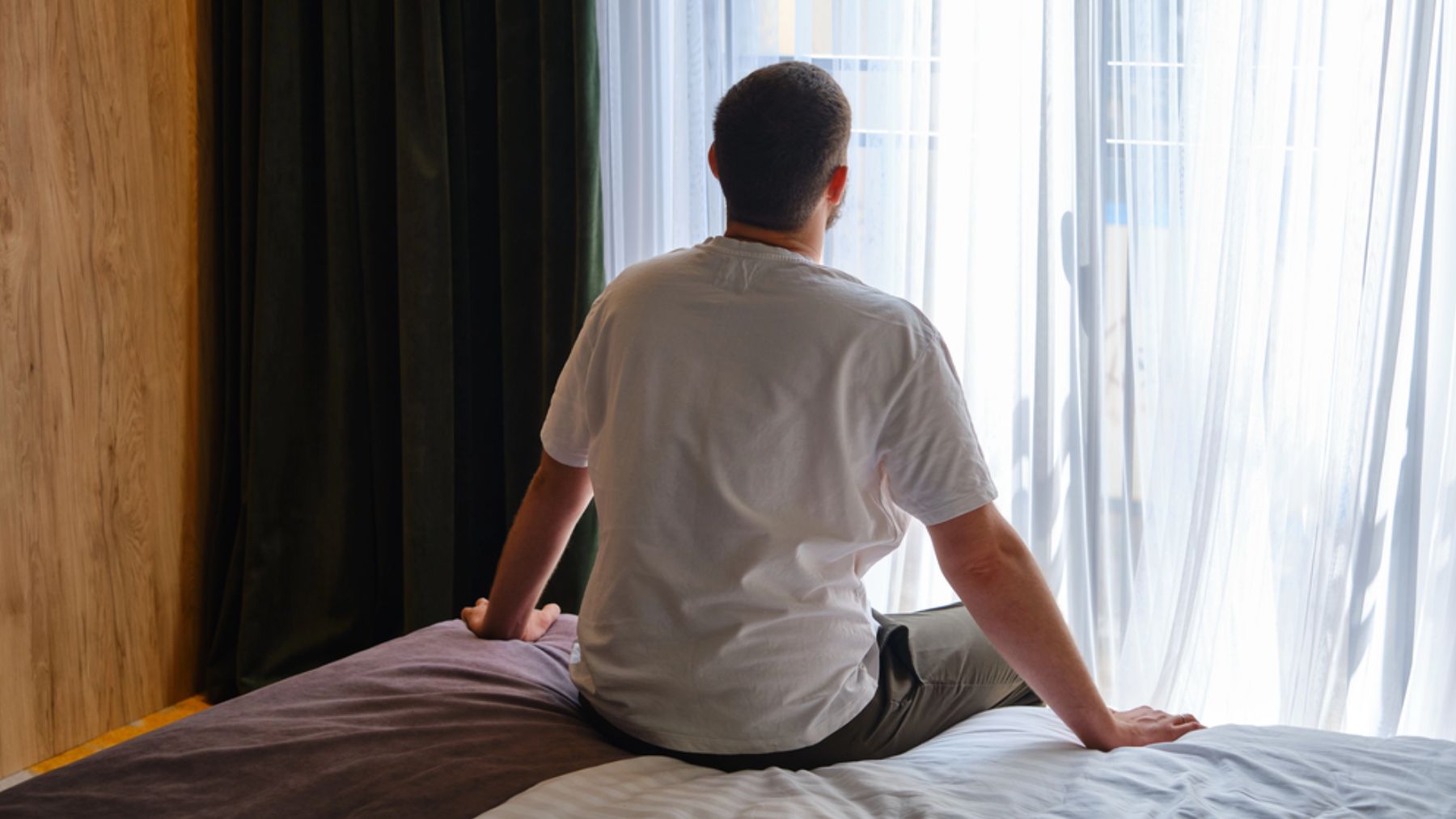 Un hombre sentado en el borde de la cama a punto de levantarse.