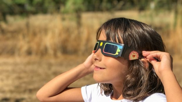 Una ni&ntilde;a peque&ntilde;a observa el sol durante un eclipse solar con unas gafas homologadas. 