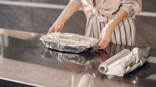 Mujer usando papel de aluminio para proteger alimentos en la cocina. (Foto: Freepik)
