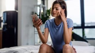 Una mujer utiliza el móvil con dolor de cabeza. Foto: Freepik