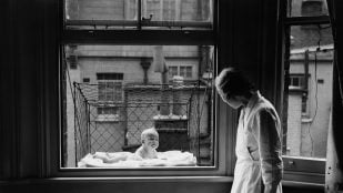Mujer observando a un bebé en una jaula. Foto de GettyImages.