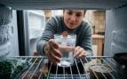 Persona colocando un vaso de agua con una moneda en el congelador (imagen hecha con IA).