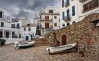 Hay lugares que consiguen mantener intacto su encanto pese al paso del tiempo y al creciente interés turístico. Hay un pueblo conocido de la Costa Brava que inspiró a Joan Manuel Serrat parar crear diversas canciones. Hoy, sigue siendo una maravilla, pero el turismo sigue en laza. Calella de Palafrugell conserva la esencia de los antiguos pueblos marineros, con casas blancas de poca altura, contraventanas de madera pintadas en verde o azul, callejuelas estrechas que desembocan en el mar y pequeñas playas de aguas transparentes. Pasear por sus rincones permite descubrir un paisaje mediterráneo que combina tradición, naturaleza y una atmósfera tranquila difícil de encontrar en otros destinos muy visitados del litoral catalán. Además de su indudable belleza, Calella de Palafrugell ofrece múltiples propuestas para disfrutar de unas vacaciones completas. Sus playas y calas invitan tanto al descanso como a la práctica de actividades acuáticas, mientras que sus senderos costeros permiten contemplar algunos de los paisajes más espectaculares de la Costa Brava. La Organización de las Naciones Unidas para la Educación, la Ciencia y la Cultura (UNESCO) destaca la importancia de preservar el patrimonio cultural y paisajístico como elemento esencial para el desarrollo sostenible de los destinos turísticos, mientras que la Comisión Europea impulsa iniciativas que fomentan un turismo respetuoso con el entorno y las comunidades locales. Qué ver en Calella de Palafrugell: el pueblo de casas blancas que inspiró a Joan Manuel Serrat Sus antiguas casas de pescadores, perfectamente conservadas, forman un conjunto histórico que refleja el pasado marinero de la población. Frente al mar se sitúan Les Voltes, una característica galería porticada con grandes arcos que se ha convertido en uno de los espacios más representativos de la Costa Brava. Bajo sus soportales se concentran restaurantes y terrazas donde degustar pescado fresco y especialidades de la cocina mediterránea. Desde Port Bo parten pequeñas calles empedradas que conducen hasta la iglesia de San Pedro, construida a finales del siglo XIX. Su fachada blanca y el gran reloj del campanario destacan entre las viviendas tradicionales del casco urbano. También merece la pena descubrir algunas construcciones singulares, como Casa Rocamora, Casa Verdaguer o Casa Sagrera, ejemplos del crecimiento residencial que experimentó la localidad sin perder su identidad arquitectónica. Playas y calas para desconectar Uno de los principales atractivos de Calella de Palafrugell son sus playas de arena dorada y sus pequeñas calas escondidas entre acantilados y pinares. Port Pelegrí, Canadell y Golfet figuran entre las más conocidas, aunque cualquier paseo por la costa permite encontrar rincones tranquilos donde disfrutar del Mediterráneo. Las aguas cristalinas convierten la zona en un lugar ideal para practicar deportes acuáticos. Entre las formaciones rocosas habitan numerosas especies marinas que pueden observarse fácilmente con unas gafas de buceo y un tubo. Quienes deseen explorar el litoral desde otra perspectiva también pueden alquilar un kayak y acceder a pequeñas calas únicamente accesibles desde el mar. El encanto del Camí de Ronda en el pueblo que inspiró a Joan Manuel Serrat El histórico Camí de Ronda constituye una de las mejores formas de descubrir el paisaje de este tramo de la Costa Brava. El sendero conecta Calella de Palafrugell con Llafranc y Cap Roig mediante un recorrido que alterna bosques de pinos, acantilados, miradores naturales y pequeñas playas. El paseo resulta apto para la mayoría de los visitantes y ofrece numerosas oportunidades para detenerse a contemplar el mar o fotografiar algunos de los rincones más emblemáticos del litoral gerundense. Durante el recorrido también se aprecia la riqueza geológica y vegetal que caracteriza esta parte del Mediterráneo. Cultura y tradiciones junto al mar Cada verano, Calella de Palafrugell se convierte en un importante escenario cultural. La Cantada d'Havaneres de Port Bo reúne desde 1967 a miles de personas para disfrutar de uno de los géneros musicales más vinculados a la tradición marinera catalana. El ambiente que se crea frente al mar convierte este evento en una experiencia difícil de olvidar. A ello se suma el Festival de Cap Roig, celebrado en los jardines botánicos del mismo nombre. Este prestigioso ciclo de conciertos reúne cada año a artistas nacionales e internacionales en un entorno privilegiado con vistas al Mediterráneo. Qué hacer en los alrededores Muy cerca de Calella se encuentran otros lugares de gran interés, como el faro y la torre de Sant Sebastià, desde donde se obtiene una panorámica excepcional de la costa. También merece una visita el Museo del Corcho de Palafrugell, dedicado a una actividad industrial que marcó durante décadas la economía de la comarca. Los aficionados a la literatura pueden acercarse a la Fundación Josep Pla para conocer mejor la obra del escritor ampurdanés, mientras que los amantes de la naturaleza disfrutarán recorriendo el espacio natural protegido de Castell-Cap Roig y sus jardines botánicos, considerados entre los más bellos del litoral catalán.