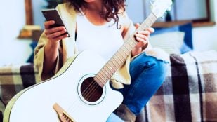 Una mujer aprende tocar la guitarra con el móvil. Foto: Freepik