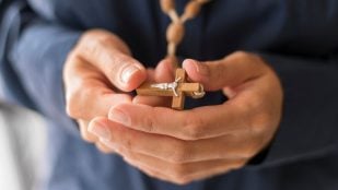 Persona sosteniendo un rosario con una cruz. Foto: Magnific