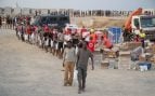 Varios inmigrantes hacen cola para que les den comida en una playa