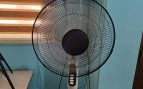 Ventilador de pie encendido junto a una ventana con persianas