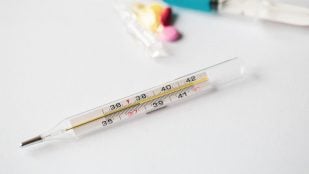 Un termómetro de mercurio marca cerca de 39 grados junto a pastillas y un frasco de medicamento. Foto: pvproductions / Freepik.