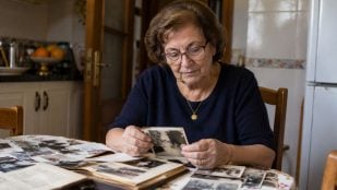 Mujer mayor nacida en los años 50 o 60 mirando fotos antiguas en una mesa, recordando la época en la que tuvo que dejar los estudios para trabajar
