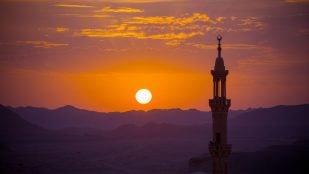 Puesta de sol sobre el desierto con el minarete de una mezquita en primer plano. Foto: Magnific - @nikitabuida