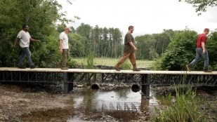 Cuatro personas cruzan el puente de 12 metros construido con cerchas de plástico reciclado de Atlas Building Composites en un humedal de Massachusetts. Foto: Cortesía de Atlas Building Composites