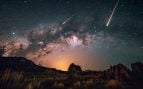 Dos meteoros cruzan un cielo nocturno con la Vía Láctea sobre un paisaje de rocas y pastizales. Foto: Magnific - @Vecstock