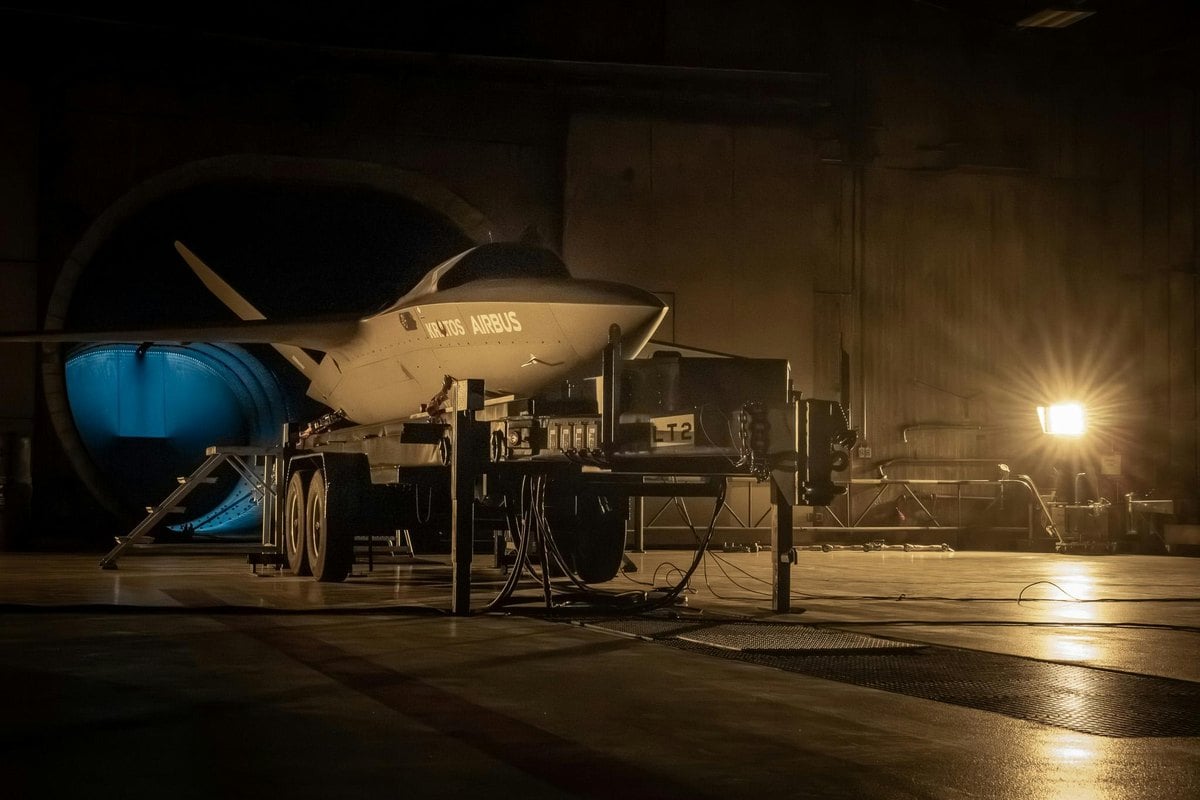Dron de combate Valkyrie con los logotipos de Kratos y Airbus sobre un soporte en un hangar