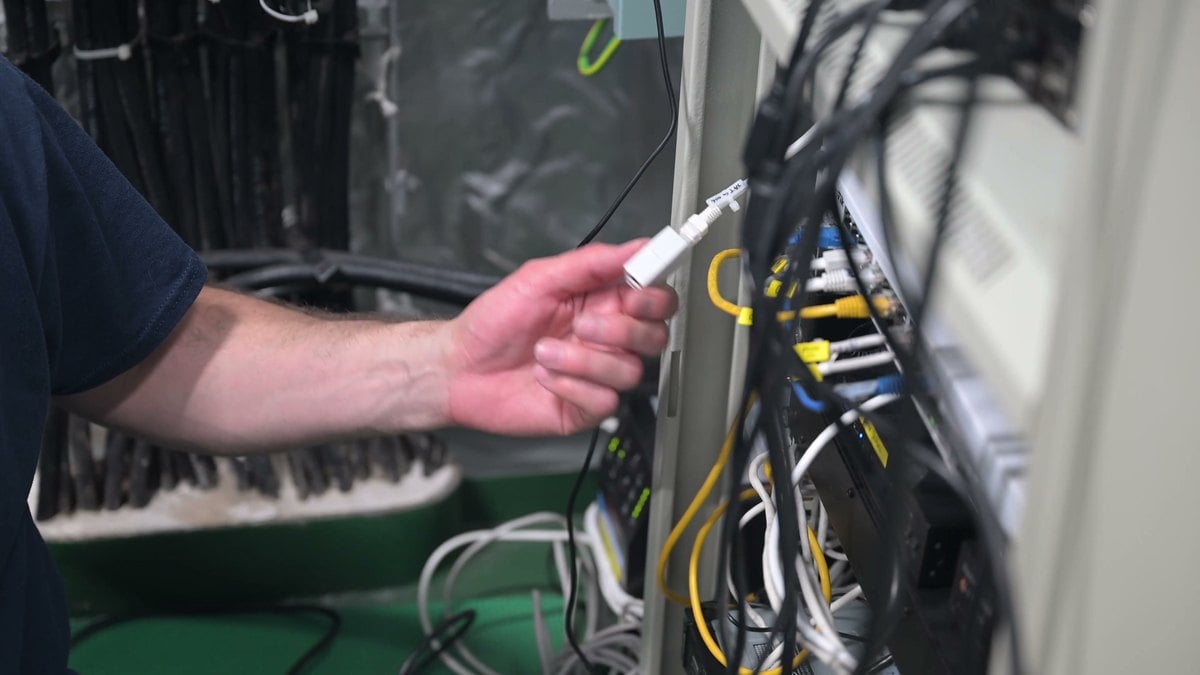 Una mano sostiene un conector junto a un armario con cables de red, en un vídeo de la Guardia Costera grabado a bordo de un buque tanque