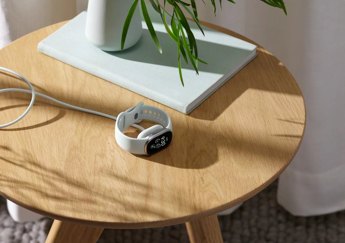 Una Google Fitbit Edge blanca carg&aacute;ndose con su cable sobre una mesa de madera