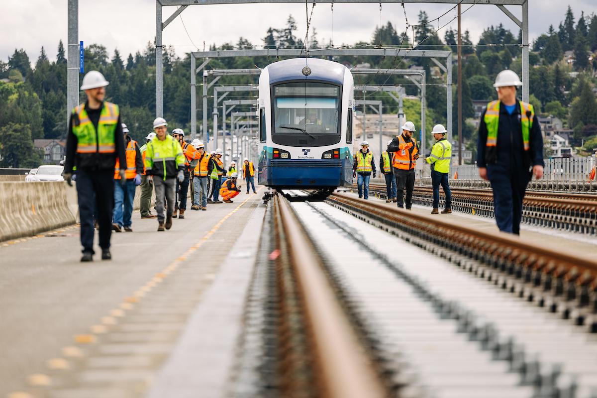 Técnicos con casco caminan junto a un tren de Link sin energía sobre las vías del puente de la I-90