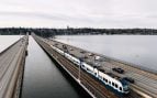 Un tren ligero de cuatro coches cruza el puente flotante de Seattle sobre el lago Washington, junto a los carriles de la I-90