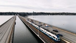 Un tren ligero de cuatro coches cruza el puente flotante de Seattle sobre el lago Washington, junto a los carriles de la I-90