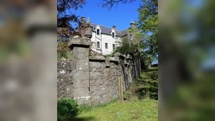 Fachada blanca del castillo Hallgreen con una torrecilla de piedra, tras un muro de piedra y un césped, en Aberdeenshire (Escocia)
