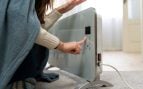 Una mujer abrigada con una manta ajusta con el dedo el panel digital de un radiador eléctrico. Foto: Magnific