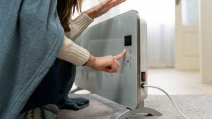Una mujer abrigada con una manta ajusta con el dedo el panel digital de un radiador eléctrico. Foto: Magnific