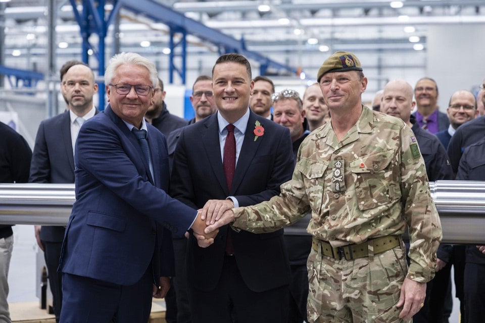 Armin Papperger, Wes Streeting y el general Roly Walker se dan la mano ante un tubo de cañón en la fábrica de cañones de Telford
