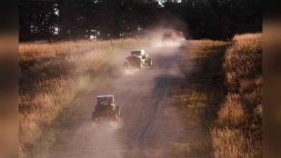 Vehículos autónomos del programa RACER de DARPA avanzan en fila por un camino de tierra en el campo de tiro St. Vith de Fort Knox