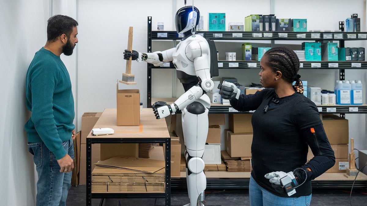 Una investigadora con guantes de sensores guía a distancia a un robot humanoide 4NE1 blanco que sujeta una pieza junto a una caja de cartón