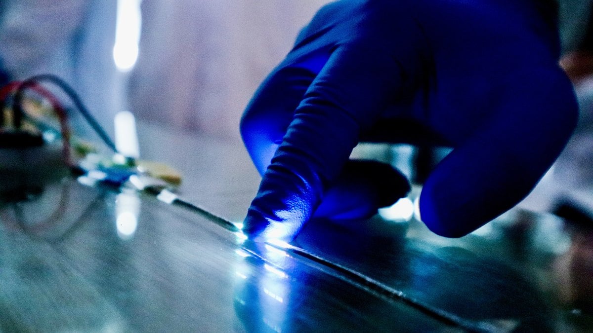 Un dedo con guante azul presiona una fibra táctil con LED encendidos en el laboratorio de la NUS