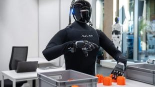 Uno de los robots humanoides de NEURA, con piel textil negra, separa piezas naranjas en una caja en la TUM RoboGym de Múnich