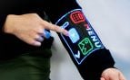 Un dedo toca la pantalla táctil de LED tejida en la manga de un jersey negro, que muestra un menú con iconos