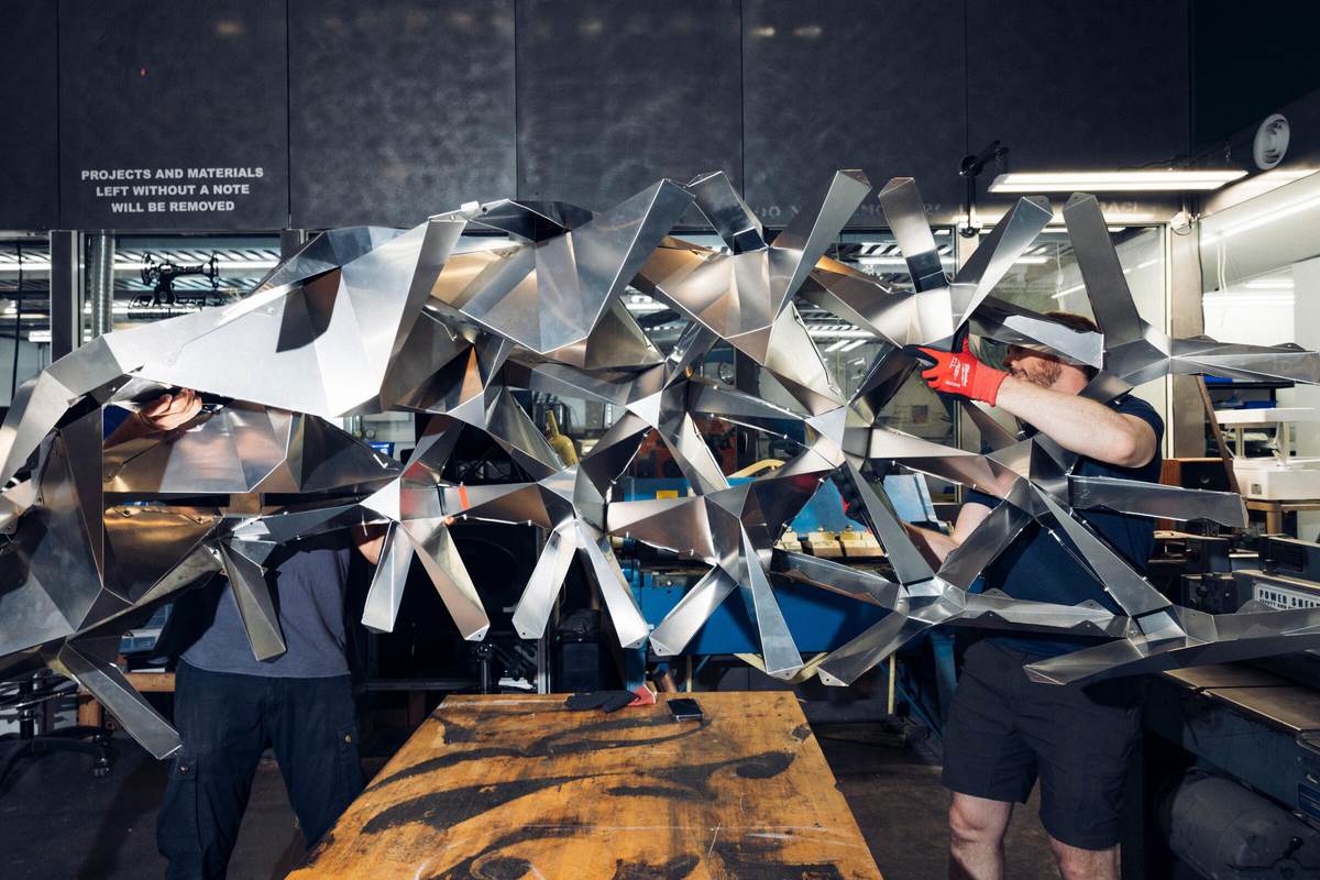Dos personas sujetan un tramo de la estructura de origami de aluminio LEXICON durante su montaje en un taller del MIT