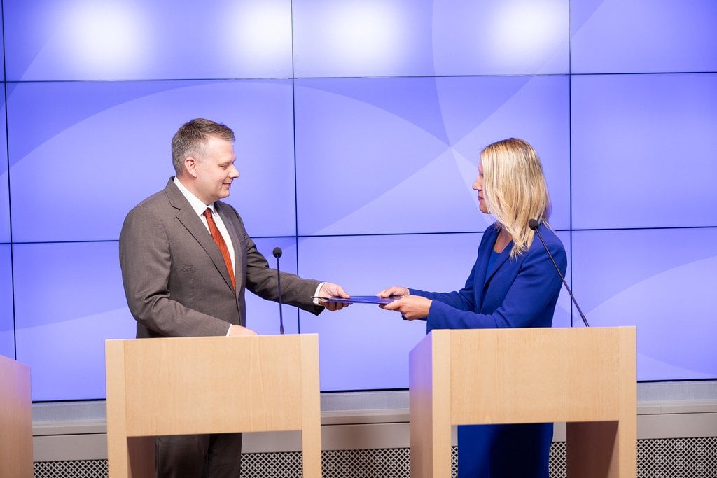La ministra finlandesa Sari Multala entrega una carpeta a Ilkka Poikolainen, consejero delegado de Posiva, en la rueda de prensa sobre la licencia del almac&eacute;n de combustible nuclear gastado