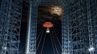 El módulo lunar Lanyue cuelga de la torre de pruebas de Huailai durante su ensayo nocturno de aterrizaje y despegue, con la Luna al fondo