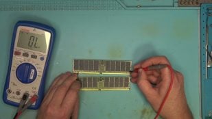 Los dos módulos de memoria RAM DDR5 de servidor de 128 GB y 256 GB sobre la mesa de trabajo mientras el técnico de northwestrepair los mide con un polímetro