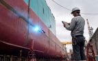Imagen conceptual de Kawasaki, no una foto real: un robot soldador de barcos con una chispa de soldadura en el casco y un operario con una tableta